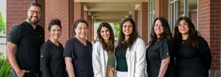 Dentists Jasmin Dhanjal And Kimia Devine standing in front of dental office with full team