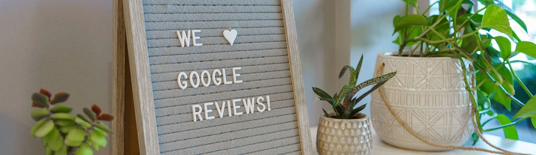 Letter board displaying We [heart] Google Reviews sitting next to decorative plants