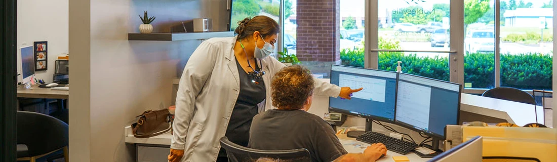 Dentist Noblesville IN Membership Plans Dental assistant pointing to computer to help front desk assistant