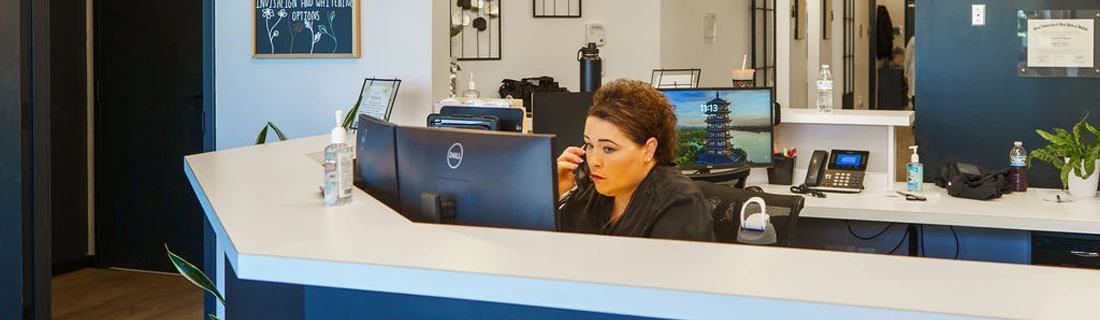 Front desk assistant sitting at computer desk while talking to a patient on the phone